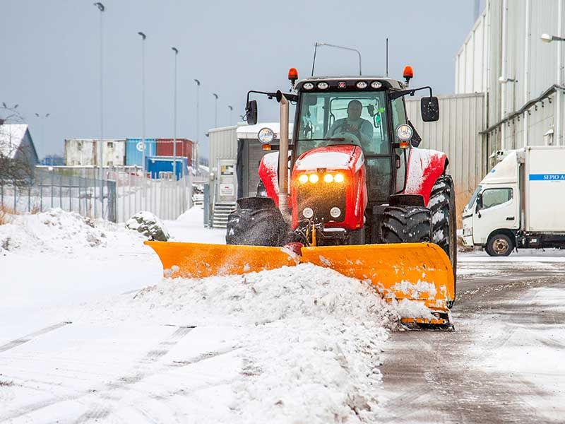 Stor rød snerydder der laver snerydning i et industrikvarter